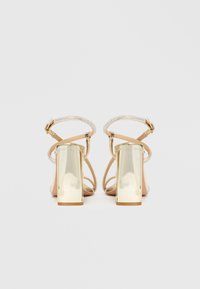 Pantofi cu toc înalt, cu barete, pe o bază nud, împodobiți cu cristale transparente și având un toc auriu, masiv, pentru stabilitate și strălucire.