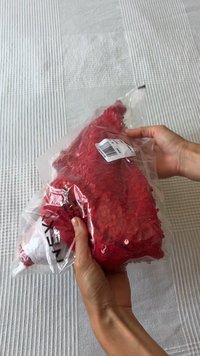 Tissu en sequins rouges maintenu dans un emballage plastique. Présente une surface texturée avec des sequins brillants, montrant une couleur vibrante et des motifs détaillés.