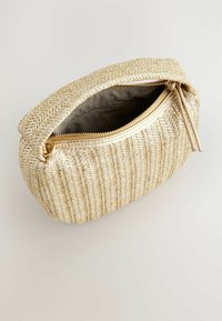 Goldfarbene gewebte Tasche mit Reißverschluss, die ein strukturiertes Design und eine offene Oberseite aufweist, vor einem hellen neutralen Hintergrund.