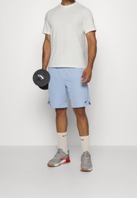 Camiseta de algodón gris claro, pantalones cortos azul claro con logo negro de Nike, zapatos grises con patrón y acentos rojos, y calcetines blancos con logo negro.