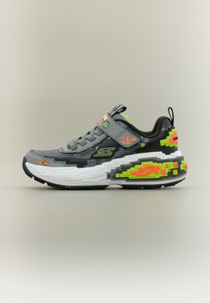 Baskets grises et noires avec motif pixélisé vert néon et orange, semelle blanche, lacets et bride Velcro sur fond uni.