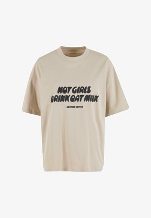 Camiseta de algodón beige con un corte holgado, escote redondo y mangas cortas. Presenta un texto gráfico en negro: "LAS CHICAS CALIENTES BEBEN LECHE DE AVENA."