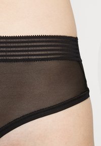 Svart mesh undertøy med en elegant design som har teksturerte horisontale striper langs midjebåndet og en myk, glatt overflate.