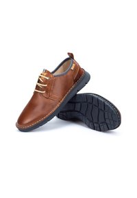 Zapatos de cuero marrón con puntera redonda, costuras claras y cordones crema. Suela de goma negra con textura para mayor agarre.