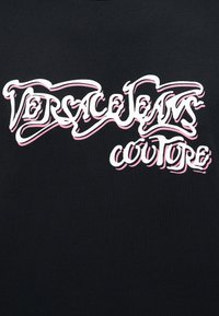 Λογότυπο Versace Jeans Couture σε λευκή γραφή με ροζ σκιά σε μαύρο φόντο.