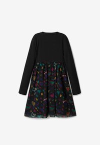 Černé šaty s dlouhým rukávem a žebrovaným vrškem, se sukní zdobenou barevným vzorem srdcí, která obsahuje různé živé odstíny na černém pozadí.