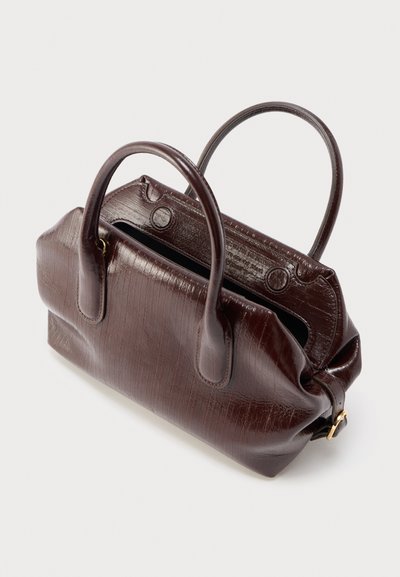 Σκούρα καφέ δερμάτινη τσάντα χειρός με διπλές στρογγυλές λαβές, χρυσή αγκράφα και ευρύ ορθογώνιο ανοιχτό πάνω μέρος πάνω σε ανοιχτό φόντο.