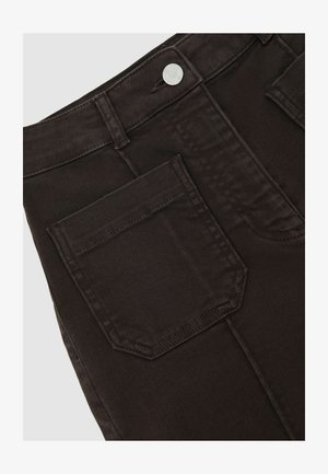 Mustade teksapükste lähivõte, kus on näha tagatasku, vööaas ja hõbedane metallist nööp vöökohal.