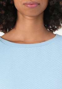Pull bleu clair texturé avec un col rond et des bordures côtelées, présentant un motif ondulé subtil sur tout le tissu.