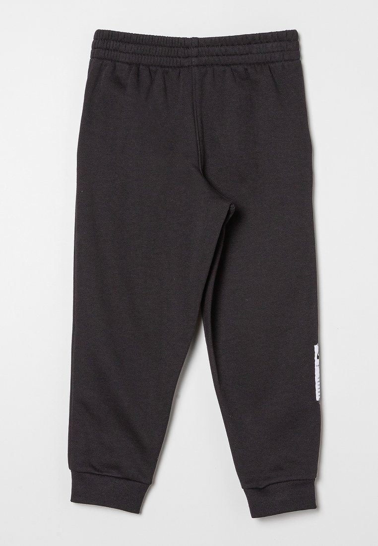 Pantalons de survêtement noirs en tissu doux, avec une taille élastique et des poignets élastiques, ornés d'une petite étiquette blanche sur le côté gauche.