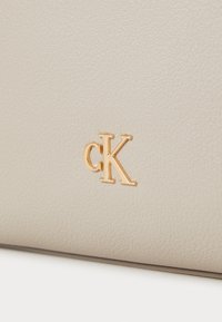 Beige faux leather bag featuring a textured surface and a gold-tone "cK" logo accent on the front.