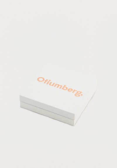 Λευκό τετράγωνο κουτί με το λογότυπο "Otiumberg." σε ροζ χρυσό, τοποθετημένο στο κέντρο του καπακιού, πάνω σε απλό λευκό φόντο.