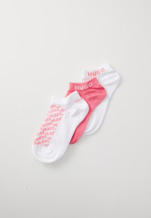 Tri para gležnjaških nogavic v beli in roza barvi. Značilnosti vključujejo logotip "HUGO" v roza barvi na belih nogavicah ter vzorčeno besedilo na roza nogavicah. Mehka material.