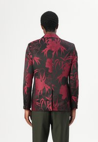 Musterblazer mit dunklem Grundton, der große rote Blumenmuster zeigt. Slim-Fit-Design mit strukturierten Schultern und einem Schlitz hinten.