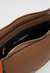 Interno di una borsa a tracolla in pelle marrone con zipper dorato, fodera nera e un compartimento più piccolo con zipper. Texture liscia con un design angolare.