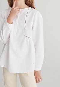 Valkoinen pitkähihaine paita napitusläpällä ja koristeommella, jossa on rento istuvuus ja hienovarainen sivuhalkio helman kohdalla.