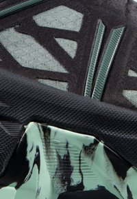 Dettaglio di sneaker nere e verde menta con una tomaia texture, ritagli geometrici e una suola a motivi in contrasto.