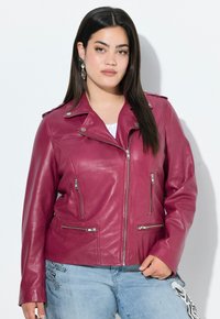 Bordeaux leren jack met ritssluitingzakken, asymmetrische ritssluiting en drukknopdetail op de kraag. G gedragen over denim met grafische accenten.