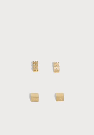 Zwei Paare goldene, quadratische Ohrstecker, eines mit kleinen klaren Steinen und beide mit dem "ck"-Logo graviert, auf weißem Hintergrund präsentiert.