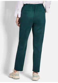 Groene, zacht aanvoelende broeken met een taps toelopend been, elastische tailleband en twee achterzakken. Draag ze met beige sneakers.