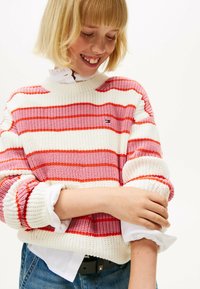Maglione a maglia con strisce orizzontali in rosso, rosa e bianco. Texture a costine con scollatura rotonda e maniche arrotolate.