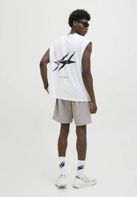 Camiseta sin mangas blanca con un diseño gráfico negro en la espalda, combinada con pantalones cortos gris claro, calcetines blancos con rayas negras y zapatillas blancas.