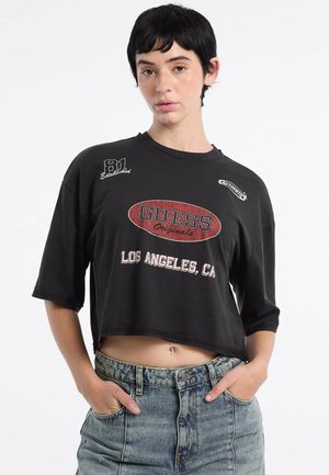 Black cropped t-shirt with a round neckline and short sleeves. Features a red "GUESS Originals" logo, textured print details, and a loose fit.