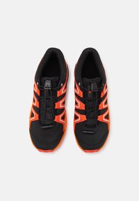 Scarpe da ginnastica nere con dettagli arancioni, tomaia in rete e tre fasce elastiche. Design leggero con una superficie strutturata e suola in gomma.