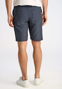 Mörkblå shorts med ett strukturerat mönster, två bakfickor med knappar och rak passform, bärs tillsammans med vita sneakers.