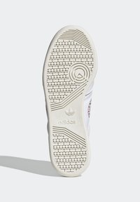 Suola di sneaker bianca con una superficie in gomma testurizzata, caratterizzata da un logo circolare sul tallone e un logo Adidas vicino all'arco.