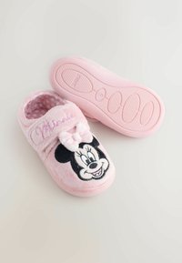Pink plush slippers featuring a Minnie Mouse design with a bow. Textured exterior and polka dot patterned lining. Soft sole for comfort.
