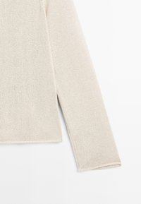 Maglione lungo beige chiaro a maniche lunghe realizzato in tessuto a maglia testurizzata, con un taglio dritto e spacchi laterali all'orlo.