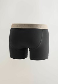 Černé boxerky s béžovým elastickým pasem, na kterém je vyraženo jméno značky "NEXT". Hladká látka, přiléhavý střih, délka do poloviny stehen.