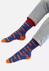 Niebieskie skarpetki z pomarańczowymi wzorami jamnika, z czerwonymi ściągaczami i pomarańczowymi palcami. Materiał wydaje się miękki i gładki w dotyku.
