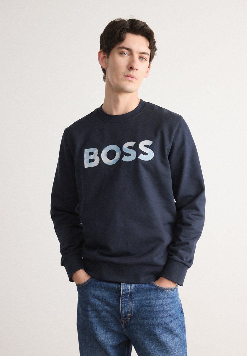 Jūras spēku crewneck svārki, kas izgatavoti no kokvilnas, ar lielu "BOSS" logotipu ombre zilu toņu salikumā krūtīs. Vienkāršs dizains bez rakstiem.