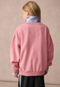 Rosa sweatshirt i mjukt tyg, med lös passform, ribbade muddar och midja. Lagen över en ljusblå skjorta med krage. Enkel design.