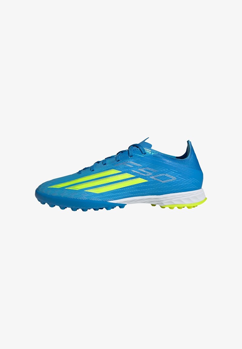 Chaussure de football bleue avec des rayures jaunes, surface texturée, lacets et semelle cloutée pour une meilleure adhérence sur herbe synthétique.
