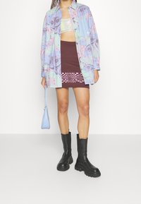 Buntes Hemd mit Augenmuster, lila Rock mit grafischem Design, schwarze klobige Stiefel und eine hellblaue Handtasche.