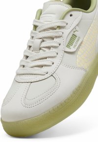 Fehér sneaker texturált zöld kiegészítőkkel és félig átlátszó talppal. Fűzős kialakítással és hangsúlyos márkalogóval rendelkezik az oldalán.