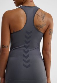 Grå sportstopp med racerback-design, vertikalt chevronmönster och mjukt, stretchy material. Utsmyckad med dekorativa tatueringar.
