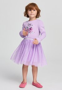 Abito lungo maniche lilla con grafica di paillettes, gonna in tulle con luccichii e vita elastica. Abbinato a scarpe basse rosa.