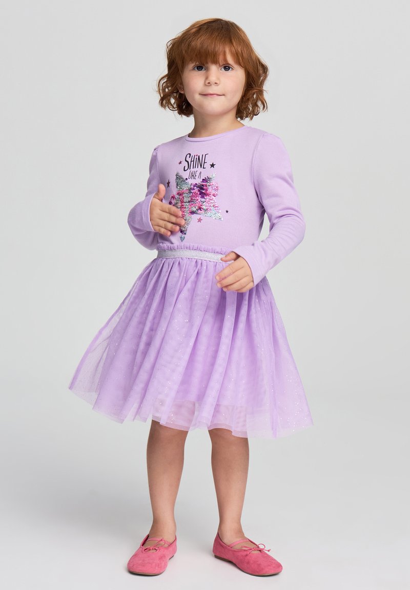 Abito lungo maniche lilla con grafica di paillettes, gonna in tulle con luccichii e vita elastica. Abbinato a scarpe basse rosa.