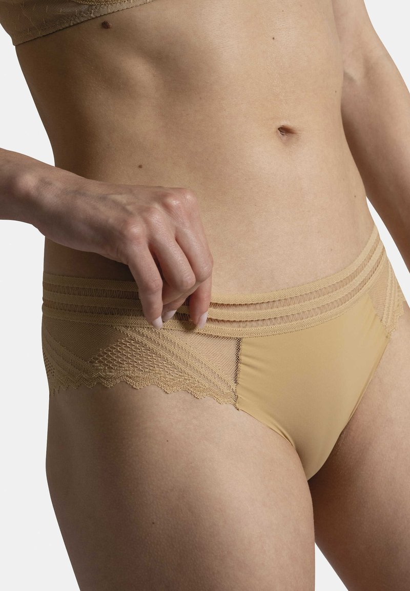 Culotte beige avec des détails en dentelle et des bords festonnés, présentant un tissu lisse et une taille texturée avec des rayures horizontales.