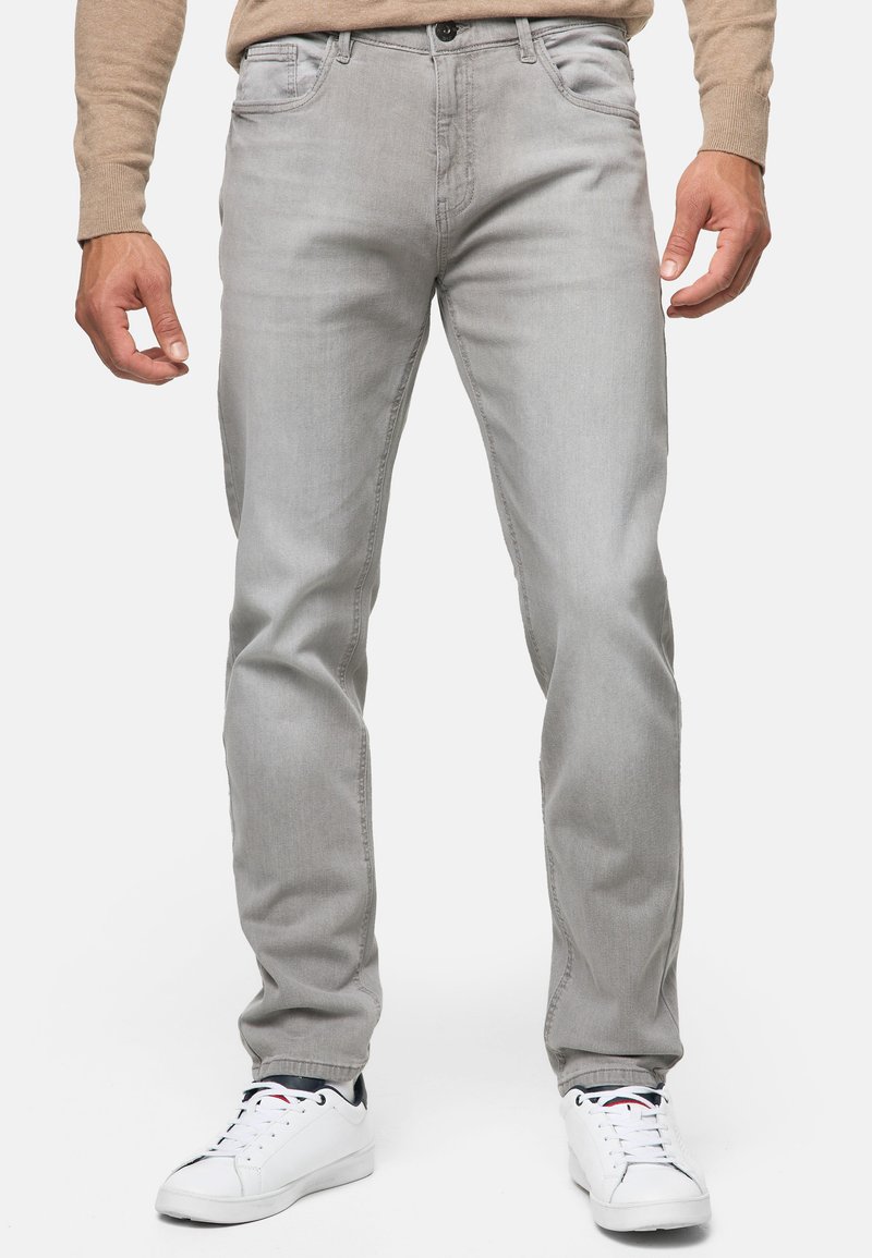 Jeans de mezclilla gris claro con corte recto, cinco bolsillos, costuras sutiles y cremallera. Combinados con zapatillas deportivas blancas.