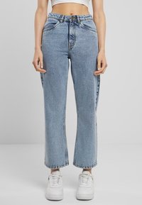 Jeans de tiro alto en azul claro con corte recto, con bolsillos frontales y cierre de botón, combinados con zapatillas blancas.