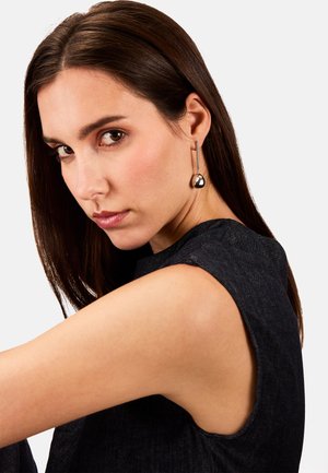 Pendientes de plata colgantes que presentan un acento metálico redondeado y una barra delgada y recta, colgando del lóbulo de la oreja, mostrando un diseño elegante.