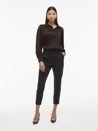 Smeđi satenasti košulja s dugim rukavima, crne krojene hlače i crne cipele s visokim potpeticama s zlatnim lancima.