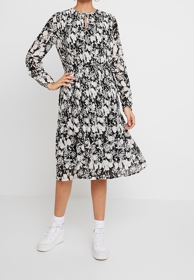Blommönstrad svartvit klänning med långa ärmar, samlad midja, nyckelhålsringning och en flödande kjol. I kombination med vita sneakers.