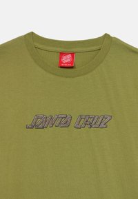 Olivgrön t-shirt med rund halsringning. Har "JANTA CRUZ"-logotyp broderad i ett trä-mönster. Lappen indikerar storlek 10-12 år.