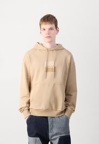Felpa beige con logo centrale, cappuccio con lacci e tasca frontale. Realizzata in tessuto morbido con polsini e orlo a costine.